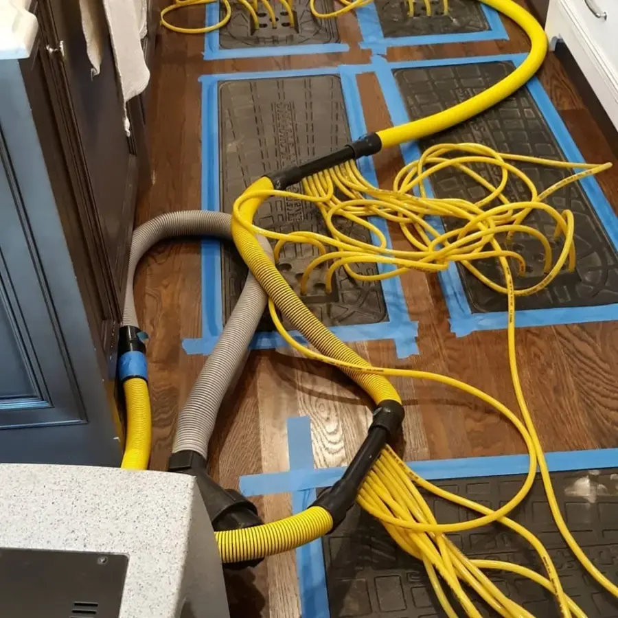 Drying mats taped over a hardwood floor with hoses running to the extraction unit