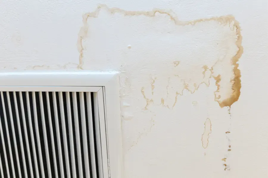 Brown water stain running down a wall beside an air return vent from an AC drain leak