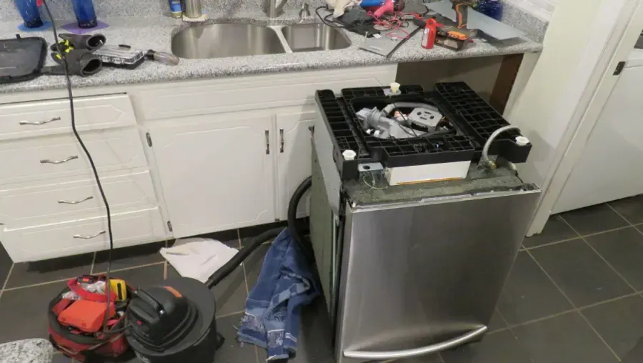 Dishwasher pulled out of a kitchen with a wet vac and hoses on the floor after a leak