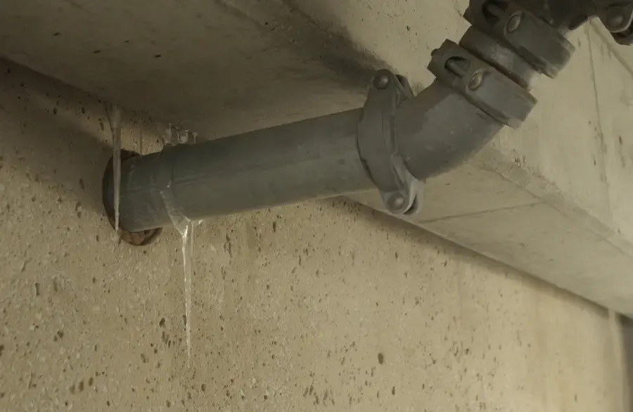 Water dripping from a cracked pipe fitting along a concrete wall after a hard freeze