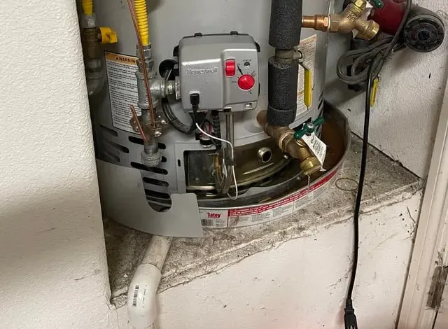 Base of a gas water heater in a closet with its drain pan and supply fittings
